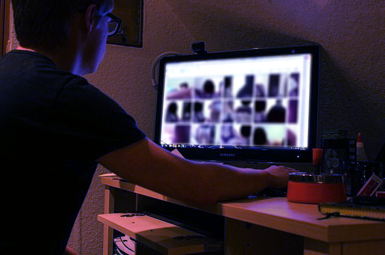 Grafika, ki prikazuje posameznika za računalniškim monitorjem in izsiljevanje z intimnimi posnetki. 