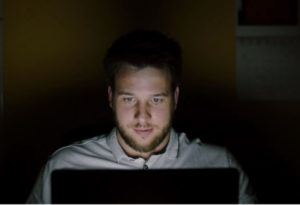 Fotografija moškega srednjih let, obraz čigar osvetljuje zaslon računalnika