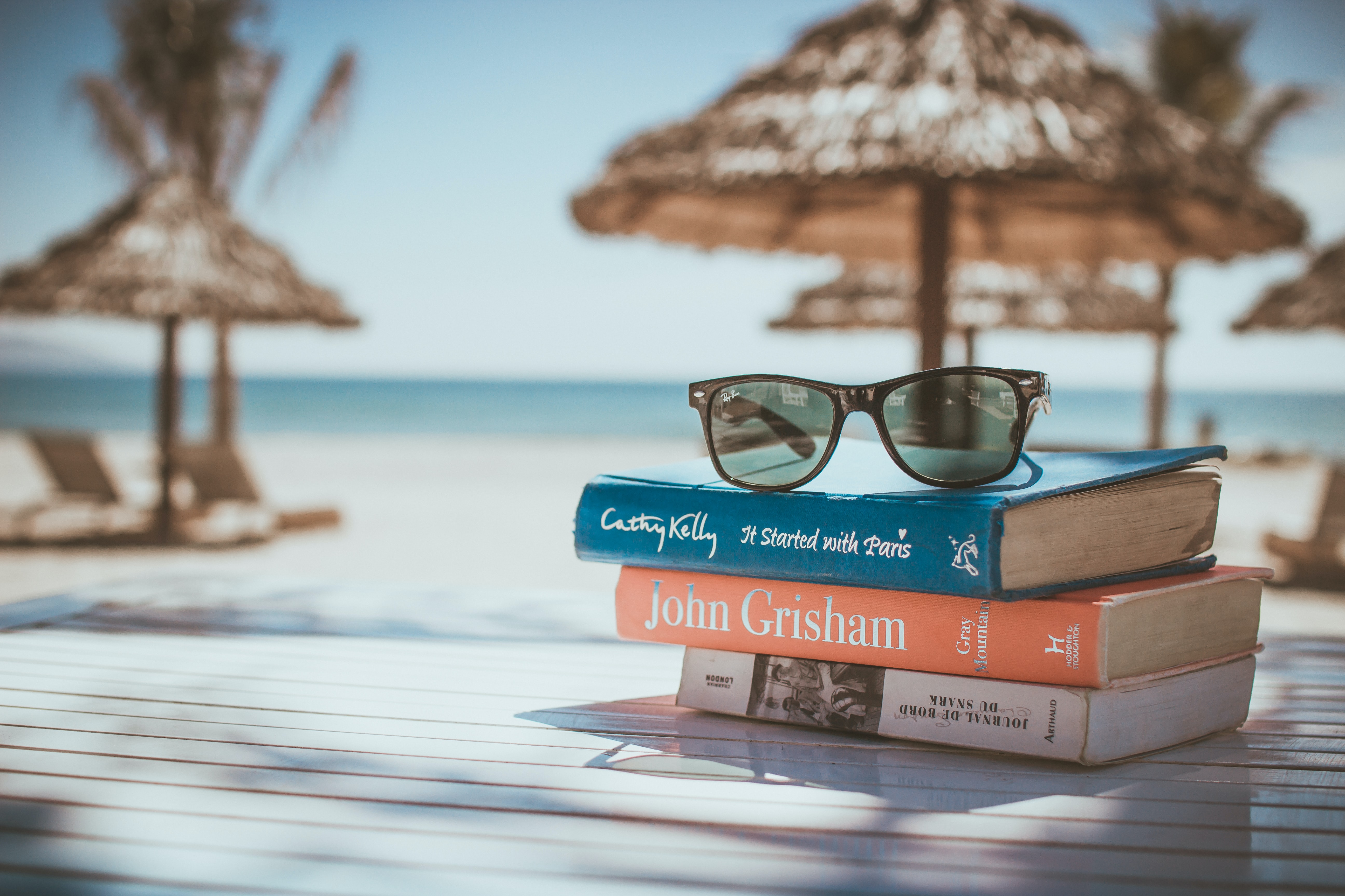 Fotografija sončnih očal na treh knjigah, v ozadju senčniki in plaža